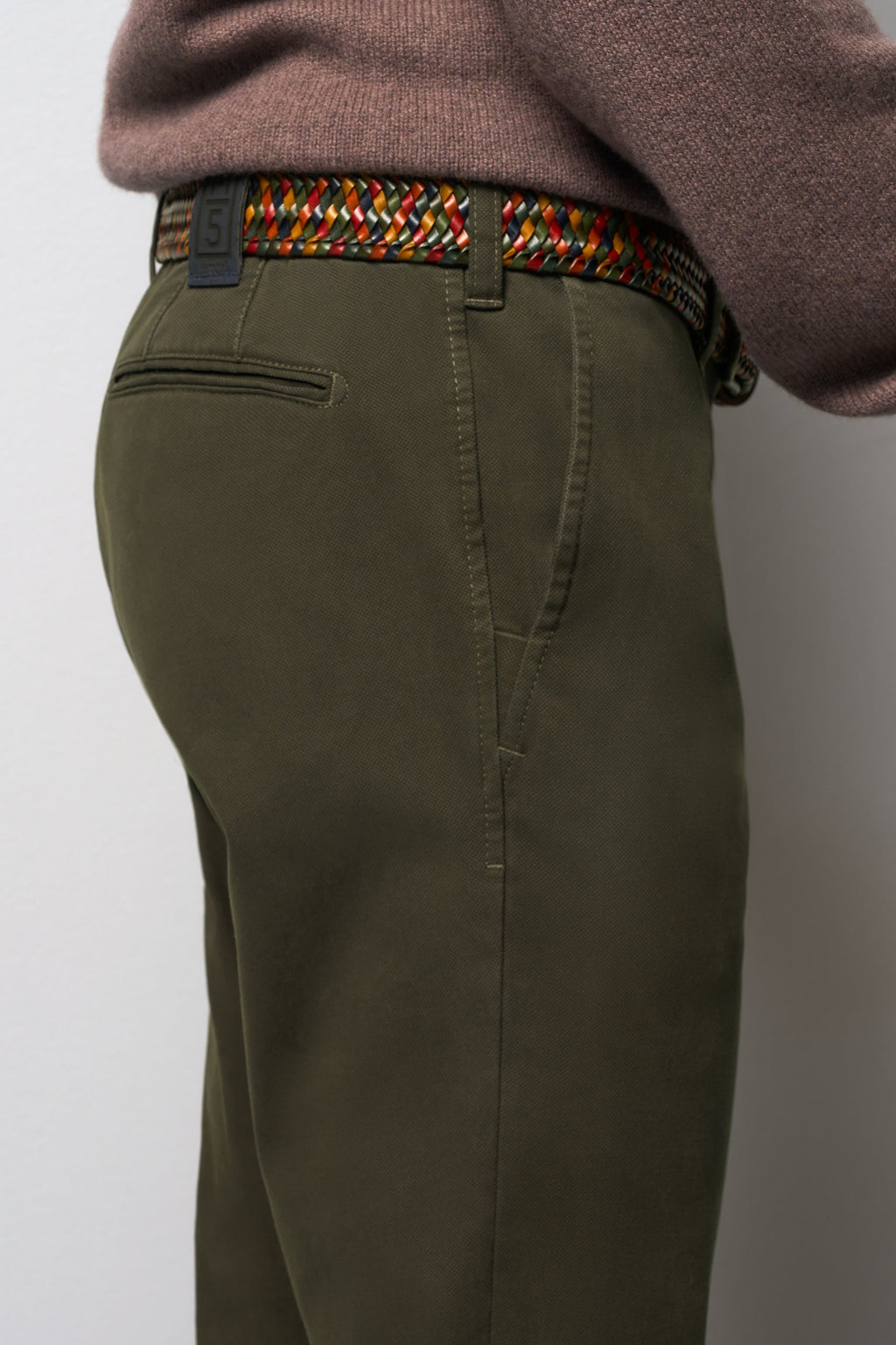 Person wearing olive green pants with a colorful belt on a plain background